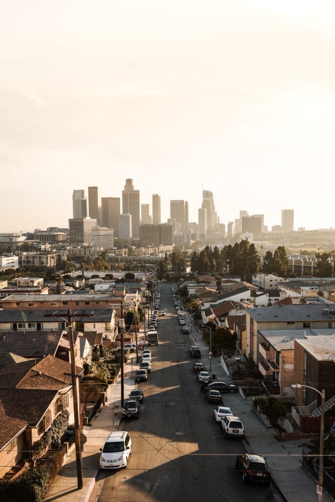 The Los Angeles skyline as seen from a distance with cars and houses of a residential neighborhood.