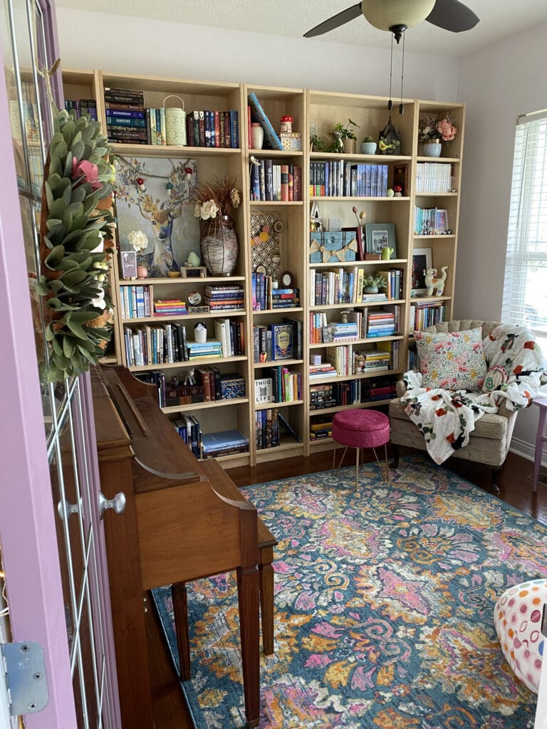 A brightly lit room with bookshelves, a piano, and an armchair wait beyond a purple door.