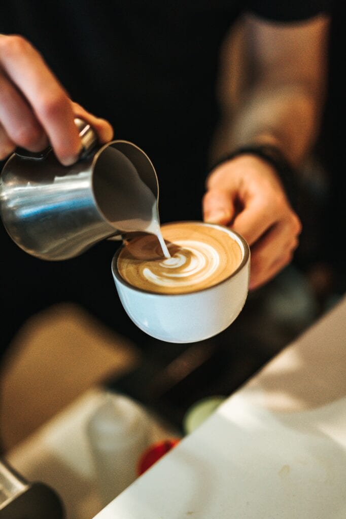 Milk being poured artfully into a small mug of coffee.